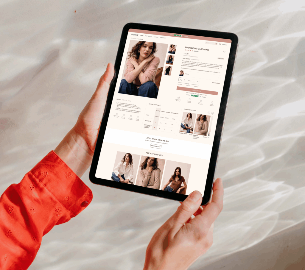 A person wearing a red long-sleeve top holds a tablet displaying an online clothing store with images and details of sweaters, similar to browsing software. The background is softly lit with abstract light patterns.